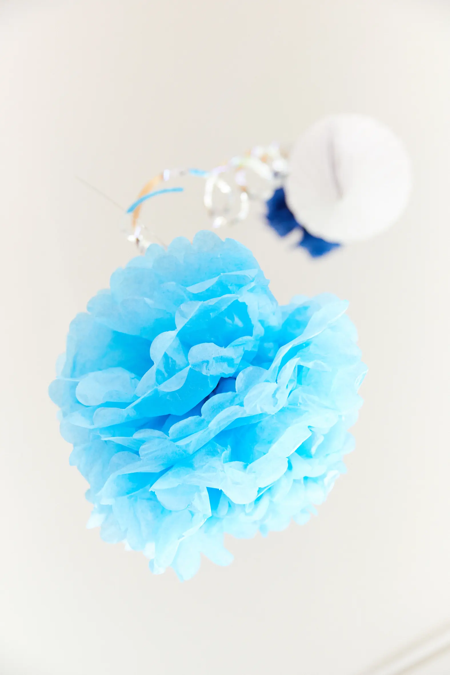 Hellblauer Papier-Pompon vor weißer Wand
