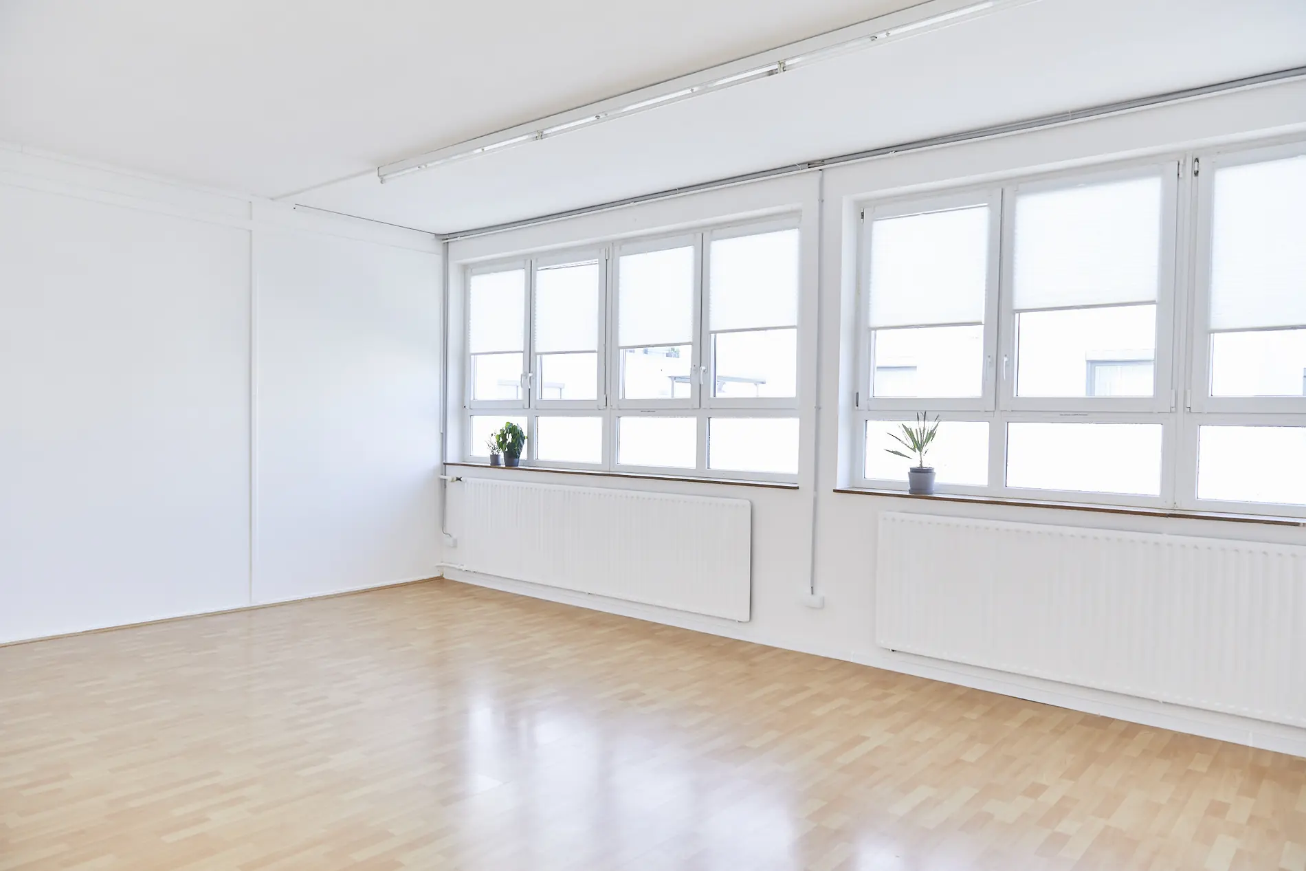 Heller, leerer Raum mit Fensterfront und Holzboden