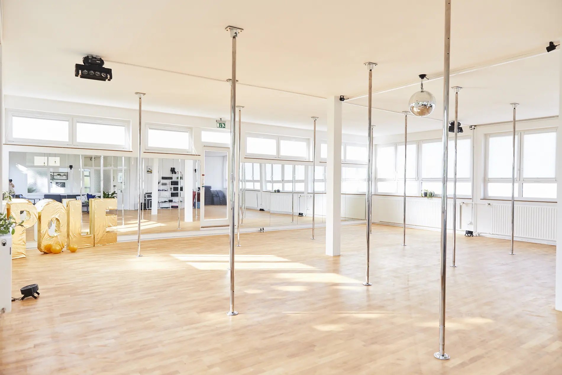 Weiter Trainingsraum mit mehreren Pole-Stangen und Parkettboden